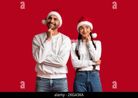 Porträt Eines Nachdenklichen Jungen Arabischen Paares In Santa Hats Mit Rotem Hintergrund Stockfoto