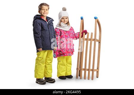 Kinder in Winterkleidung stehen mit einem Holzschlitten isoliert auf weißem Hintergrund Stockfoto