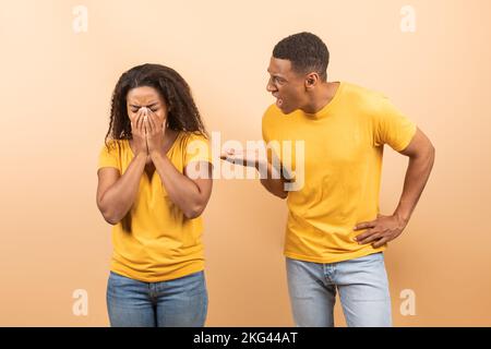 Häusliche Konflikte. Junge schwarze Ehepartner streiten sich, weinende Frau verhüllt ihr Gesicht mit Händen, während ein Mann sie anschuldet Stockfoto