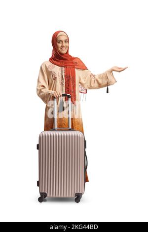 In voller Länge Porträt einer jungen Frau in ethnischen Kleidern und Hijab mit einem Koffer zeigt mit Hand isoliert auf weißem Hintergrund Stockfoto