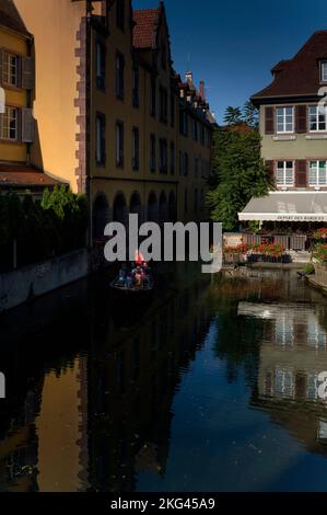 Am Abend des August nimmt die Sonne eine Barke mit flachem Boden auf und nimmt sie mit auf eine geführte Tour durch das malerische Viertel Little Venice (La Petite Venise) in Colmar, Elsass, Grand Est, Frankreich. Die Barken, die den Fluss Lauch befahren, wurden einst von den Marktgärtnern und Weinbauern genutzt, die einst das Gebiet von Krutenau bis zu den halbländlichen Vororten der Stadt besiedelten. Stockfoto