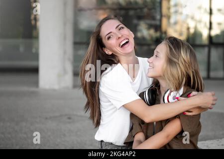 Mutter umarmt sich mit der Tochter im Freien. Fröhlicher Teenager und Frau in guter Laune. Liebe und Familienkonzept Stockfoto