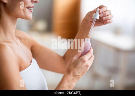 Schönheitsbehandlung zu Hause. Glückliche Frau mittleren Alters, die die Flasche mit feuchtigkeitsspendendem Serum öffnete und morgens Eingriffe machte Stockfoto