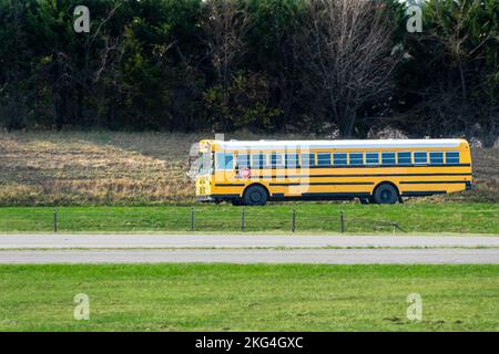 Horizontale Aufnahme eines langen Schulbusses auf einer leeren Straße. Hitzewellen erzeugen einen leichten Welleneffekt Stockfoto