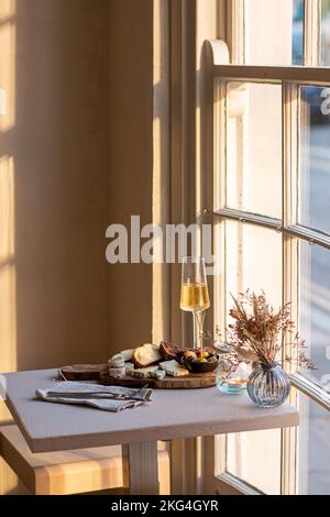 Eine vertikale Aufnahme verschiedener Käsesorten, Brot auf einem Holztablett und ein Glas Champagner auf einem Tisch Stockfoto