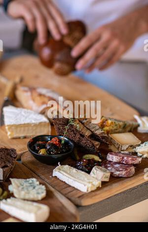 Eine vertikale Aufnahme männlicher Hände, die verschiedene Käsesorten und Brot auf einem Holztablett servierten Stockfoto