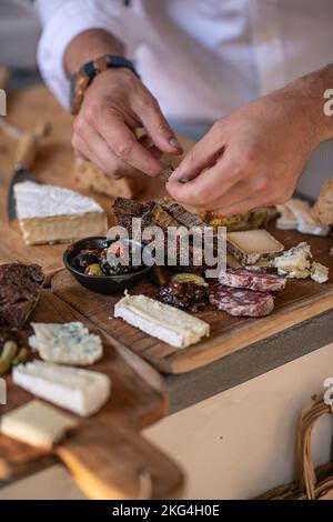 Eine vertikale Aufnahme männlicher Hände, die verschiedene Käsesorten und Brot auf einem Holztablett servierten Stockfoto