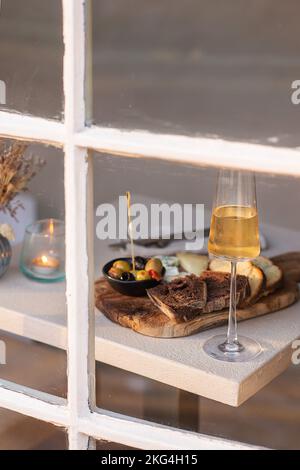 Eine vertikale Aufnahme verschiedener Käsesorten, Brot auf einem Holztablett und ein Glas Champagner auf einem Tisch Stockfoto