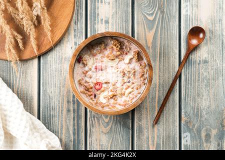 Holzschüssel gefüllt mit Vollkorngranola mit Beeren und Nüssen gefüllt mit Milch. Leckeres und gesundes Frühstück. Tablett mit Stacheln, Löffel und Stockfoto