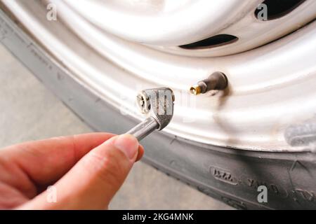 Der Fahrer pumpt einen Autoreifen mit einem Metallluftreifen-Spannfutter in der Autowerkstatt auf. Stockfoto