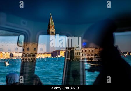 Ein Fährmann fährt mit einer Fähre durch die riesigen Kanäle von venedig. Dieses ungewöhnliche Bild zeigt den Markusplatz, den Kapitän, die atemberaubende Aussicht und Boote Stockfoto