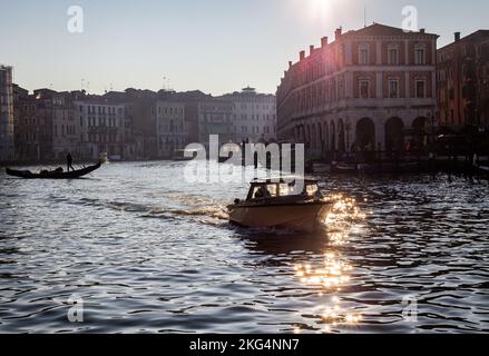 Am frühen Morgen scheint Licht durch den Canale Grande, Venedig. Ein kleines privates Motorboot fährt in Richtung Kamera und eine Gondel überquert den Kanal Stockfoto