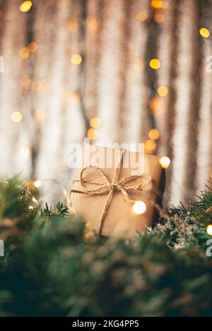 Geschenkbox aus Kraftkarton mit rauem Juteseil auf grauem Holzhintergrund mit Zweigen von Weihnachtsbäumen und Weihnachtsdekorationen Stockfoto