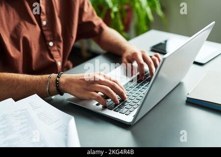 Nahaufnahme der Hände eines jungen Studenten, der auf der Laptop-Tastatur tippt, während er am Arbeitsplatz sitzt und einen Online-Grammatiktest durchführt Stockfoto