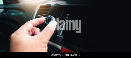 Die Fahrerhand dreht die Lautstärke des Auto-Musik-Players oder Radios auf oder ab, Panorama-Banner mit Kopierfläche auf schwarzem Hintergrund Stockfoto