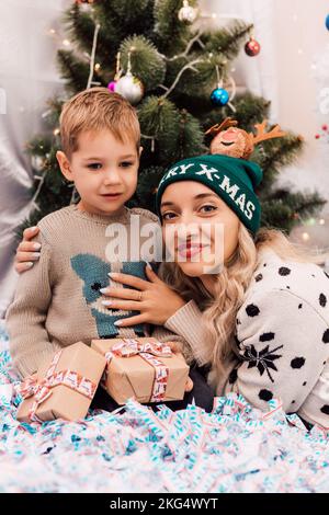 Mutter und Sohn tauschen Geschenke in der Nähe des Weihnachtsbaums aus. Weihnachtsgeschenke Stockfoto