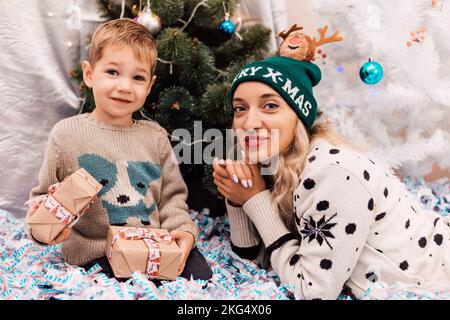 Mutter und Sohn tauschen Geschenke in der Nähe des Weihnachtsbaums aus. Weihnachtsgeschenke Stockfoto