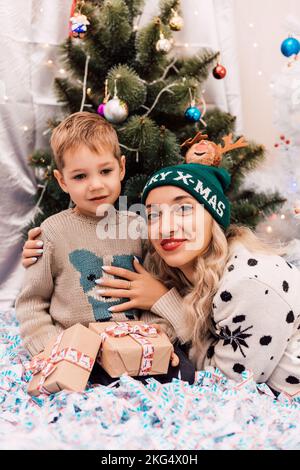 Mutter und Sohn tauschen Geschenke in der Nähe des Weihnachtsbaums aus. Weihnachtsgeschenke Stockfoto