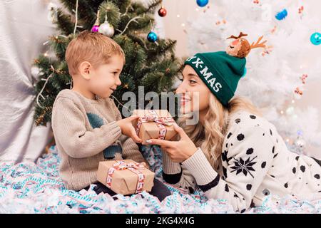 Mutter und Sohn tauschen Geschenke in der Nähe des Weihnachtsbaums aus. Weihnachtsgeschenke Stockfoto