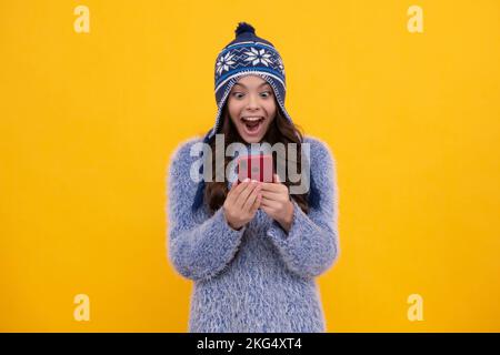 Teenager mit Strickmütze, die ihr Handy benutzt, im Internet chattet. Mobile App für Smartphone. Lifestyle-Konzept für Kinder. Aufgeregtes Teenager-Mädchen. Stockfoto