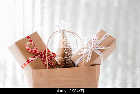 Weihnachtskomposition. Einfache Einkaufstasche voller weihnachtsgeschenkschachteln, verpackt in Kunsthandwerkpapier. Weihnachtsangebot. Modell, Raum für Ihren Text kopieren Stockfoto