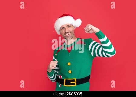 Glücklicher Mann im Elf Kostüm. weihnachtsmann im weihnachtsmann Hut auf rotem Hintergrund. Frohes neues Jahr. Stockfoto