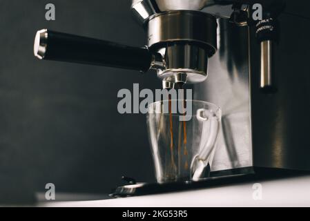 Kaffee aus dem Portafilter tropft in eine transparente Tasse. Stockfoto