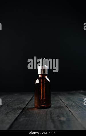 Braune Flasche für Aromaöle auf schwarzem Holzhintergrund. Stockfoto