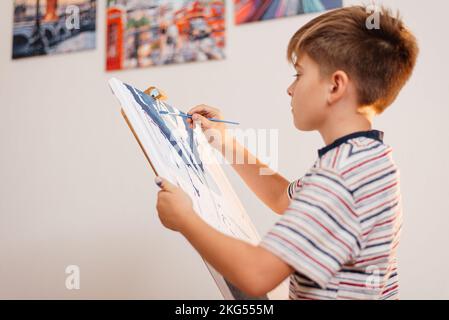 Der Junge zeichnet mit Begeisterung ein Bild mit Zahlen und einem Pinsel Stockfoto