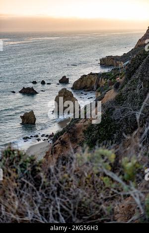 Eine vertikale Aufnahme von Felsen und Klippen am El Matador Beach Malibu mit Wellen, die die Küste während des Sonnenuntergangs waschen Stockfoto