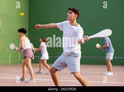 Junger männlicher Pelotaspieler trifft Ball mit Holzschläger Stockfoto