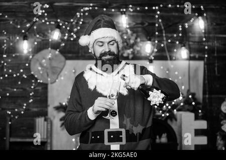 Sei glücklich. champagnerflasche vom weihnachtsmann. Winterfeier. Winterferien. Warte auf Weihnachtsgeschenke. Frohe Weihnachten. Mann, der weihnachtsmann-Hut. Neujahrsgeschenke Stockfoto