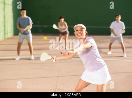 Junge hispanische weibliche Pelotaspielerin schwingt Holzpaleta, um den Ball zu treffen Stockfoto