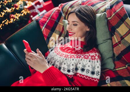 Foto einer jungen, zufriedenen, chillenden Frau im Neujahrsurlaub, die Videos auf youtube ansieht Relax while Weekend Sofa Kissen Xmas gemütliche Atmosphäre drinnen Stockfoto