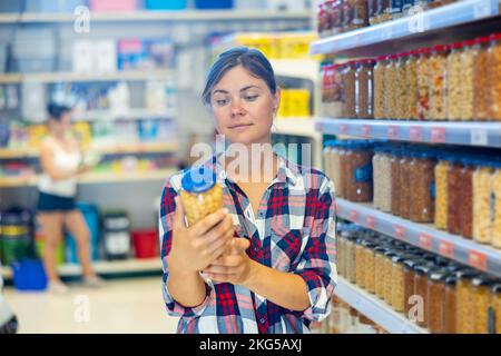 Junge Frau, die im Supermarkt Bohnen aus der Dose im Glas auswählt Stockfoto