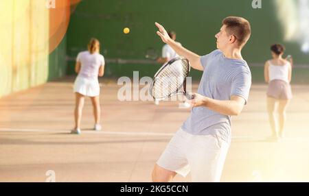 Männlicher Sportler, der sich mit Schläger auf den Ball vorbereitet. Frontenis-Spiel auf dem Platz im Freien Stockfoto