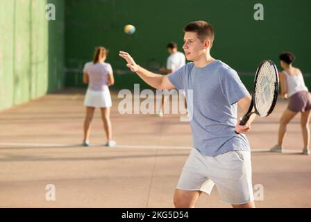 Junger männlicher Pelotaspieler trifft Ball mit Schläger Stockfoto