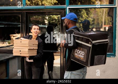 Lächelnde Kundin, die Pizzabestellung vom Kurier im Freien erhält, Frau, die den Stapel mit Essenspaketen für Kollegen nimmt. Ein afroamerikanischer Mann, der Essen zum Mitnehmen bringt, und einen Lieferservice Stockfoto