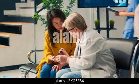 Verschiedene Frauen, die mit dem Glukometer im Wartebereich in der Lobby Insulin-Spiegel-Test machen, Diabetesuntersuchungen durchführen, um Glukose aus der Blutprobe zu messen. Arzt und Patient beim Kontrollbesuch. Stockfoto