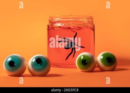 Halloween-Hintergrund mit Augäpfeln und schwarzer Spinne im orangefarbenen Gelgefäß Stockfoto