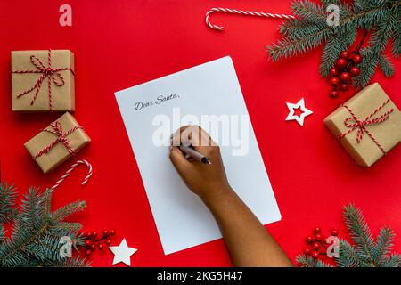 Frauenhände schreiben einen Brief an den Weihnachtsmann mit einem Weihnachtsdekorationshintergrund Stockfoto