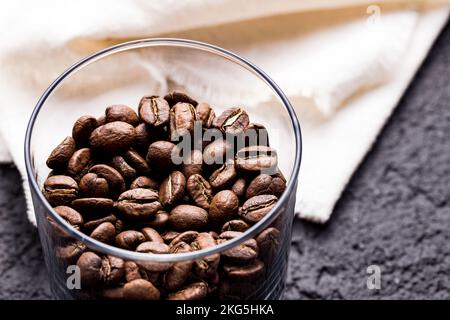 Geröstete Kaffeebohnen in Glasbehälter, auf dunklem Hintergrund, Nahaufnahme, Platz für Text Stockfoto