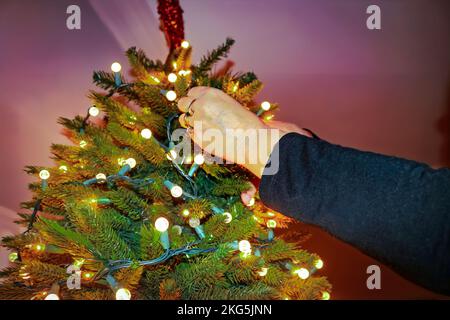 Frauenhände mit Ringen kittrige elektrische Lichter auf künstlichem Weihnachtsbaum - Nahaufnahme und selektiver Fokus Stockfoto