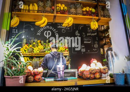 01-03-2018 Athen Griechenland - Fruchtsaftstand unter freiem Himmel mit männlichem Kellner und Obsthaufen - strahlende Sonne Stockfoto