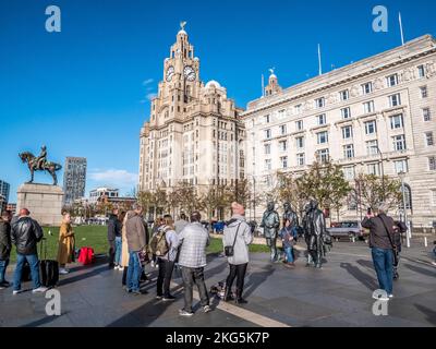 Straßenszene in Liverpool mit Touristen, die sich anstellen, um Selfies mit den Statuen der berühmten Beatles Pop-Gruppe und dem Liver Building zu machen Stockfoto