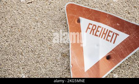 3D-Darstellung eines zerkratzten Dreiecksschilds mit Inschrift „Freedom“ auf deutscher Sprache auf Asphalt Stockfoto