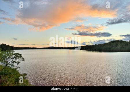 Die Sonnenuntergangswolken strahlen ein warmes Licht auf die ruhige Oberfläche eines Grubensees auf der Iron Range in Minnesota Stockfoto