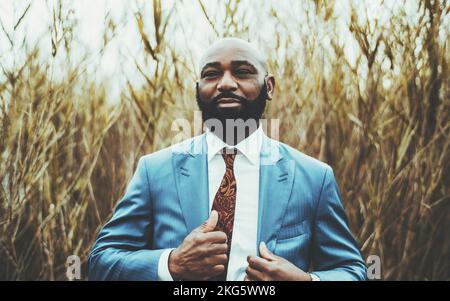 Das Porträt eines modernen, kahlköpfigen, reifen schwarzen Unternehmertums mit dickem Bart und einem eleganten blauen Anzug mit Krawatte passt den Blazer-Whi an Stockfoto