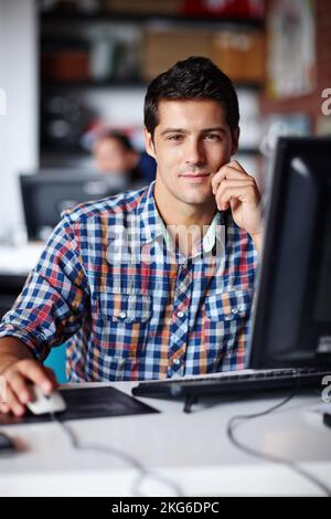 Kreativ und entschlossen - junger Designer. Porträt eines hübschen jungen Designers, der im Büro an seinem Schreibtisch sitzt. Stockfoto