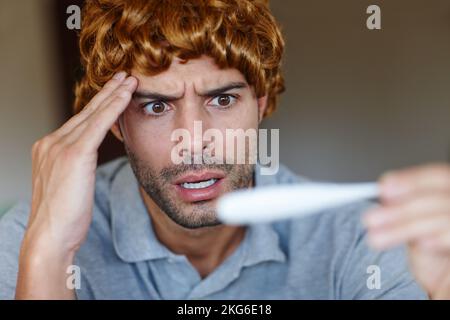 Das ist unmöglich. Ein schockierter Mann, der eine Perücke trägt und seine Temperatur auf einem Thermometer abliest. Stockfoto